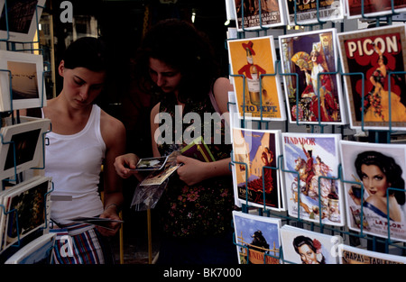 Due turisti femmina foglia attraverso vari cartoline al di fuori di un negozio nel centro di Siviglia, Spagna. Foto Stock