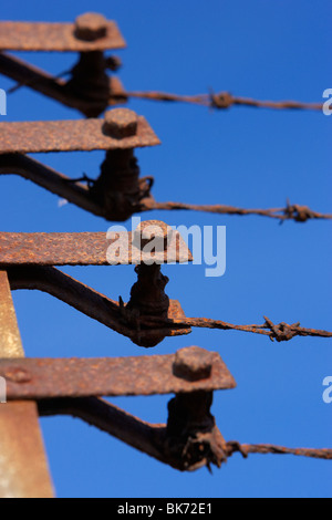 Vecchio arrugginito arrugginita fine tenditori posti di un filo spinato recinto di sicurezza contro un cielo blu Foto Stock