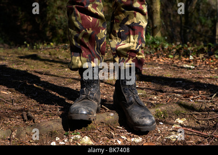 Uomo che indossa il camuffamento combattere i pantaloni e stivali in piedi in una foresta nel Regno Unito Foto Stock