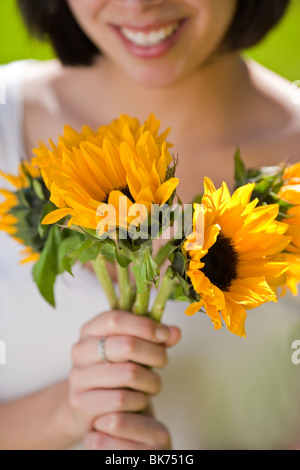 Bella, giovane donna ispanica in un prato erboso tenendo i fiori Foto Stock