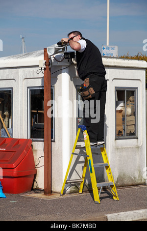 Ingegnere uomo in piedi su scala a gradini che lavora sul sistema CCTV al porto dei traghetti di Lymington, Lymington, Hampshire UK nel mese di aprile Foto Stock