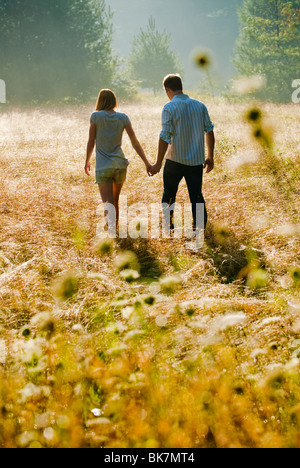 Coppia giovane camminare attraverso il campo tenendo le mani Foto Stock