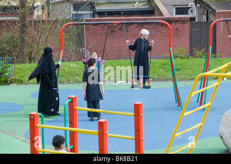 I musulmani compresi una donna in un burkha in un parco giochi in una zona musulmana di Blackburn Lancashire, Regno Unito. Foto Stock