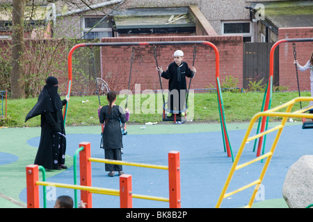 I musulmani compresi una donna in un burkha in un parco giochi in una zona musulmana di Blackburn Lancashire, Regno Unito. Foto Stock