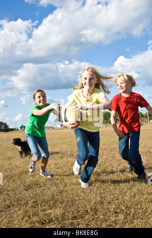 Un gruppo di ridere i bambini a giocare con un cane e un campo di calcio Foto Stock