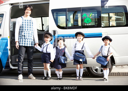 Insegnante di scuola materna e bambini in piedi nella parte anteriore del bus di scuola Foto Stock