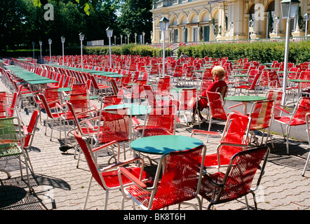 Lone donna che indossa un maglione rosso seduti a un outdoor cafe red sedia, Bundesgarten, Burggarten, Hofburg di Vienna, Austria Foto Stock