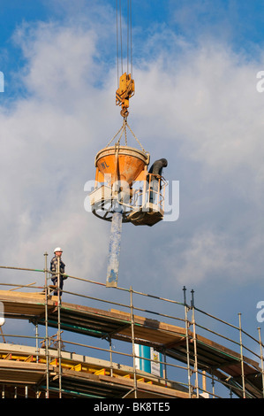 Operaio edile in piedi su una benna di calcestruzzo e il tubo flessibile che si abbassa per un sito in costruzione Foto Stock