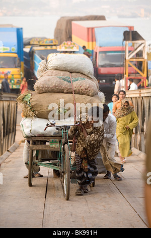 Un rickshaw conducente tira il suo carico pesante fino il gangplank dopo lo sbarco da un traghetto sul Fiume Karnaphuli, Chittagong Foto Stock