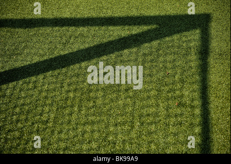 Un ombra da un obiettivo di hockey net brilla su di un verde esterno astro turf. Foto Stock