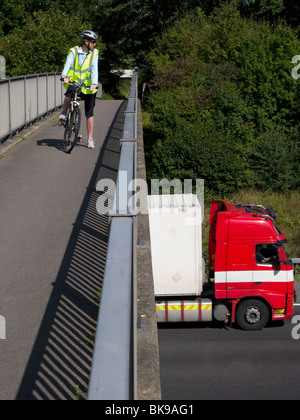 Ciclista su un pedone / / ciclo passerella guarda giù sul camion / traffico che viaggia su M25 autostrada nr Leatherhead. Surrey, Regno Unito Foto Stock