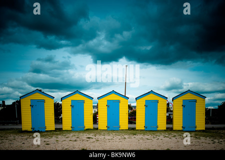 Giallo e blu cabine sulla spiaggia, sotto un cielo moody sulla spiaggia di LITTLEHAMPTON, WEST SUSSEX Foto Stock