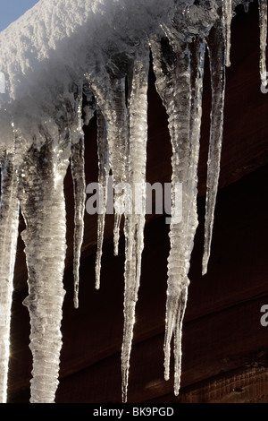 Neve e ghiaccioli pendenti dal tetto della costruzione in legno Foto Stock