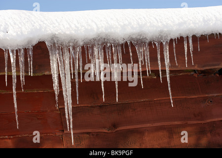 Neve e ghiaccioli pendenti dal tetto della costruzione in legno Foto Stock