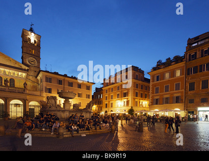 La gente seduta sui gradini di una fontana, la chiesa di Santa Maria in Trastevere in background, Roma, Italia Foto Stock