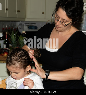 Madre utilizzando Hedrin trattamento per figlie pidocchi della testa Foto Stock