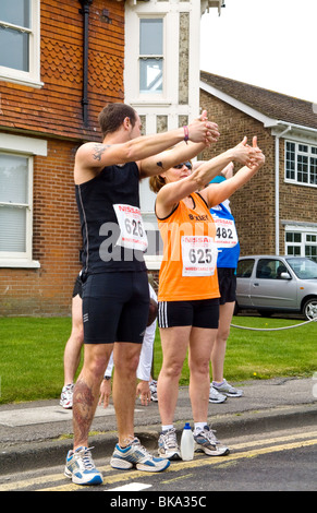 I corridori che allunga in strada prima di iniziare a 10km di corsa di beneficenza e con il loro 10k i numeri di gara che mostra. Foto Stock