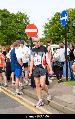 Grande folla di persone e alcuni corridori in attesa per l'inizio di una 10km corsa di beneficenza e con i loro numeri di gara che mostra. Foto Stock