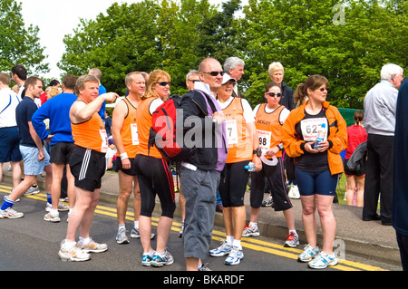 Gruppo di corridori la raccolta in strada prima di iniziare a 10km carità eseguire guardando qualcosa nella distanza con il loro 10k i numeri di gara che mostra. Foto Stock