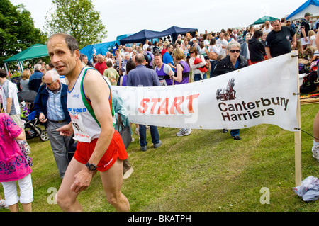 Grande folla di persone e alcuni corridori in attesa vicino all'inizio segno del Canterbury Harriers 10km corsa di beneficenza e con il loro 10k i numeri di gara che mostra. Foto Stock