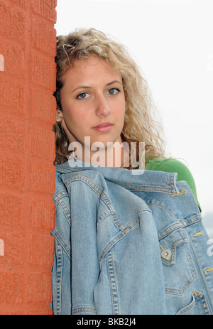 Un triste caucasian ragazza adolescente si appoggia contro un edificio in mattoni. Foto Stock