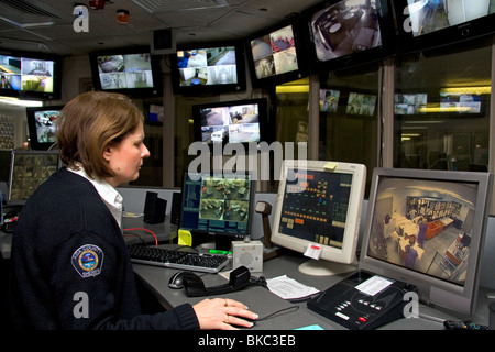 Carcere sala di controllo per la sicurezza con la femmina officer utilizzando video monitora e controlla in remoto le porte. Foto Stock