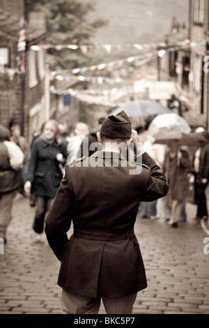 Un uomo in costume trattiene il suo cappello come egli cammina giù per una strada di ciottoli durante un 1940s evento in Haworth, Regno Unito Foto Stock