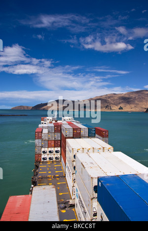 Vista del mazzo impilato con contenitori come nave naviga il canale del porto sul suo cammino al mare. Foto Stock