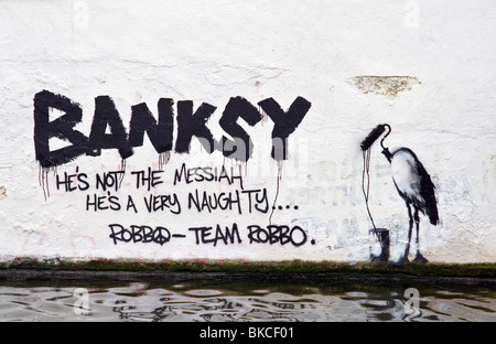 Banksy graffiti su un dipinto di bianco muro di mattoni sul lato di Regents Canal vicino a Camden Lock North London REGNO UNITO Foto Stock