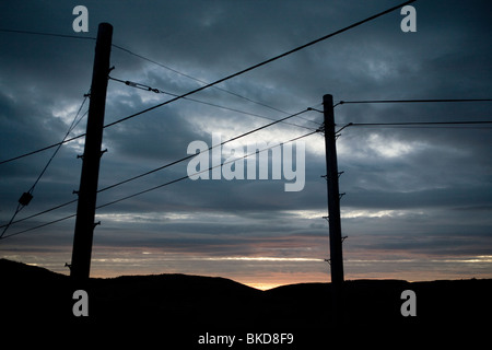 Tramonto e stagliano le linee elettriche di alimentazione in Galles. Foto Stock