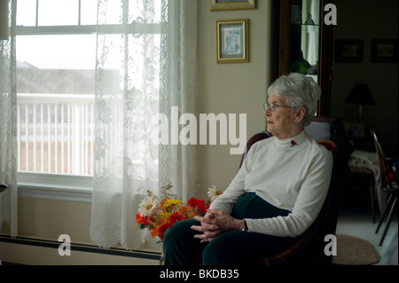 Il vecchio donna guarda avanti mentre è seduto in salotto sedia Foto Stock