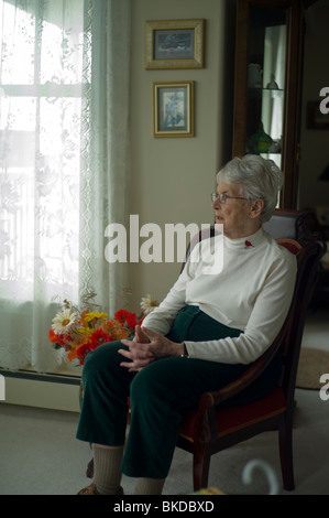 Il vecchio donna guarda avanti mentre è seduto in salotto sedia Foto Stock