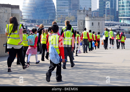 Vista posteriore della gita scolastica bambini e adulti che indossano abiti da giubbotto ad alta visibilità in gita scolastica a piedi verso la Torre di Londra Inghilterra Regno Unito Foto Stock