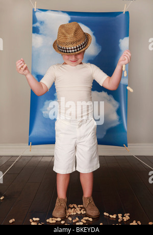 Ragazzo in hat giocando con arachidi nella parte anteriore del cielo blu e nuvole Foto Stock