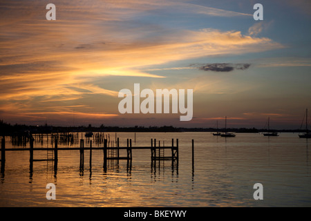 Mares tails nubi in un profondo arancione tramonto con palificazioni nell'acqua. Foto Stock