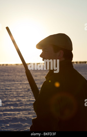 Una silhouette di uomo fagiani di ripresa in un campo di neve Foto Stock