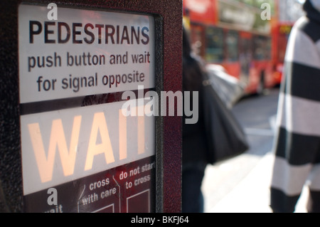 Pedonale illuminato 'IN ATTESA' firmare in corrispondenza di un incrocio occupato, Oxford Street London REGNO UNITO con un bus rosso nella messa a fuoco morbida dello sfondo Foto Stock