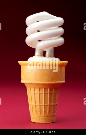 Una lampada compatta a fluorescenza in un cono gelato su rosso Foto Stock