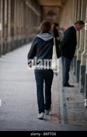 Male Teen Walking Away, da dietro, nel colonnato nel "Jardin du Palais Royale", Parigi, Francia Foto Stock