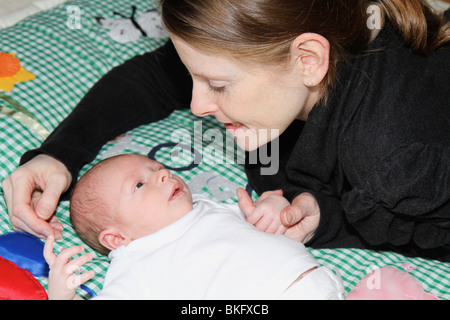 La madre e il neonato ragazzo su un tappeto gioco cercando in ogni altri occhi la madre è consolante il bambino tenendo le mani Foto Stock