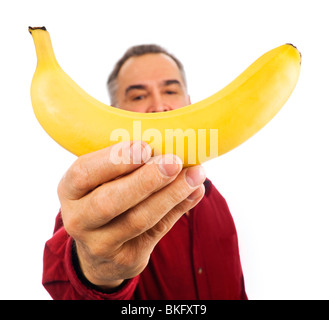 Uomo maturo detiene una banana matura con un braccio teso, di fronte al suo volto. Imita un sorriso, con la faccia al di fuori della messa a fuoco. Foto Stock