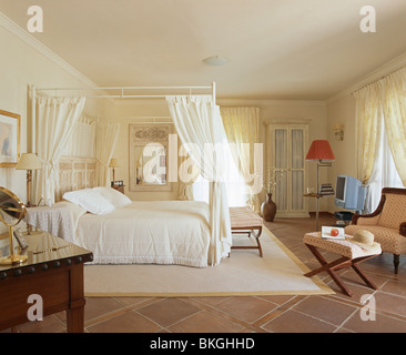 Drappi bianchi e sulla biancheria da letto semplice a baldacchino in spagnolo camera da letto con crema tappeto sul pavimento piastrellato Foto Stock