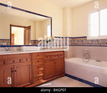 Grande specchio sopra in legno in dotazione unità vanity in spagnolo moderno bagno con piastrelle a motivi geometrici sopra bordo vasca da bagno Foto Stock