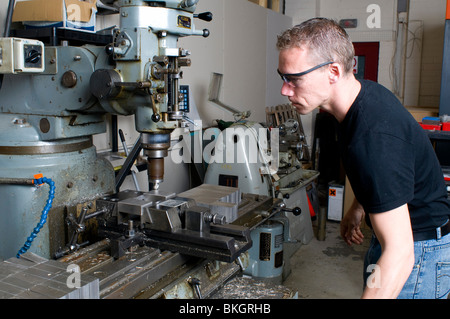 Un ingegnere di precisione nella sua bottega utilizzando una macchina di fresatura che indossa gli occhiali di protezione. Foto Stock