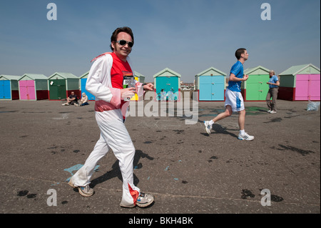 Un runner vestito come Elvis costeggia cabine sulla spiaggia, sul lungomare a Hove negli ultimi chilometri della maratona di Brighton Foto Stock