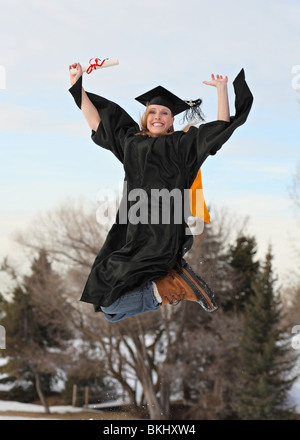 Excited donna bionda in abito di graduazione e diploma all'aperto in inverno il salto in aria in alto Foto Stock