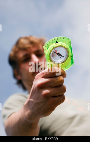 Young Millennial man hiker navigating looking at and using navigation orienteering hiking compass in hand to point right direction ahead. UK Britain Foto Stock