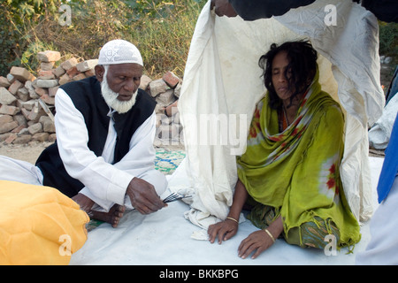 Un Sufi uomo santo o Pir, esorcizza lo spirito da una donna ad una dargah o santuario nella parte Sud di Delhi, India Foto Stock