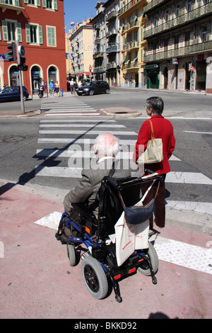 Disabledold uomo seduto in un elettrico sedia a rotelle in attesa di un segnale stradale davanti una zebra Attraversamento linea,nice,Francia Foto Stock