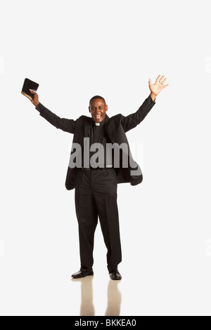 Un uomo che indossa un collare clericale e tenendo una Bibbia con le mani alzate Foto Stock